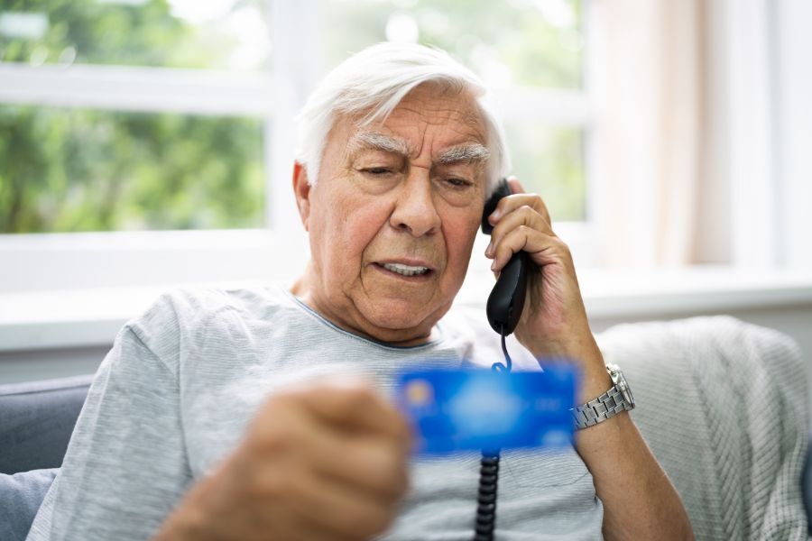 An elderly man on the telephone, holding and reading his bank card