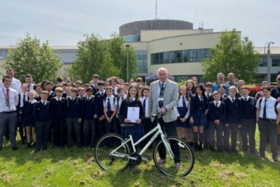Councillor Stuart Hughes, and lots of young people, all stood outside a school. Cllr Hughes is holding a bike
