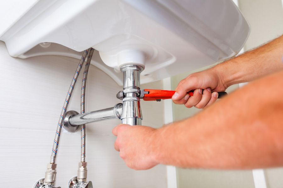 A plumber (arms only) seen fixing the underside of a sink