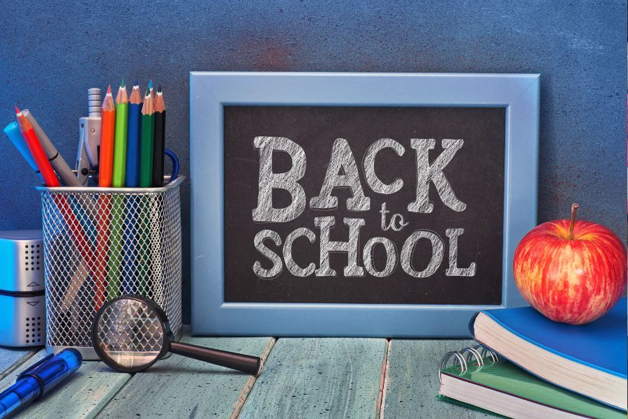 An image showing a black board with the words 'Back to School' behind a pile of school books and equipment