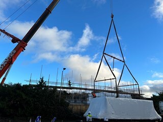 Modular houses wrapped in protective white covering being lifted into place by a crane.