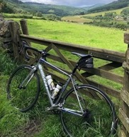 Bike against a gate with grass and fields behind, with a view of a wooded valley