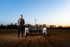 Man standing in a field next to a agricultural robot.