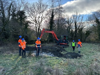 People and a digger standing around a wide hole in the ground