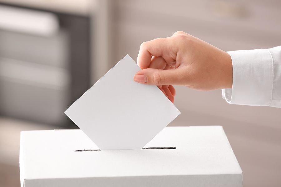 A hand posting a ballot slip into a ballot box