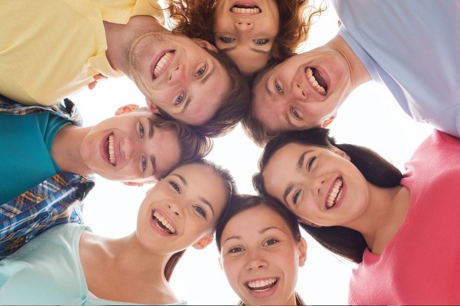 A group of teenagers stood in a circle, heads together, looking and smiling down at the camera
