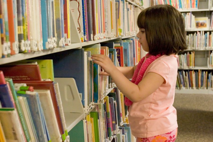 young girl looking at books in library