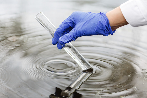 Someone gathering water from a river using a test-tube