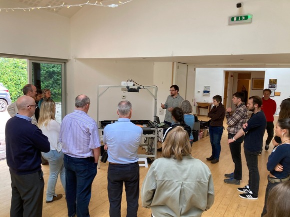 Group of people standing in a semi-circle listening to a demonstration being given of a sandbox table