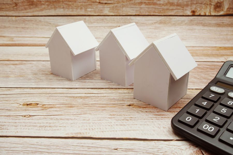 three small model houses sat by a calculator on a desk