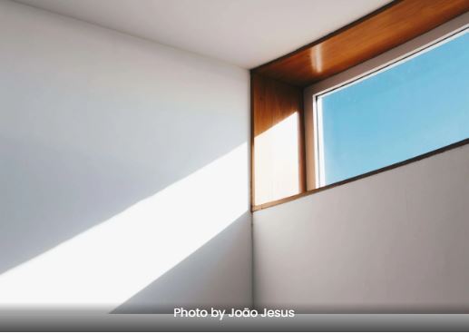 A high window in a white room with blue sky and sun seen through the window.