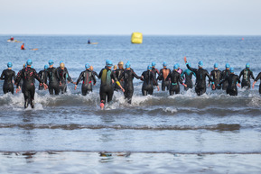 people in wetsuits running into the sea