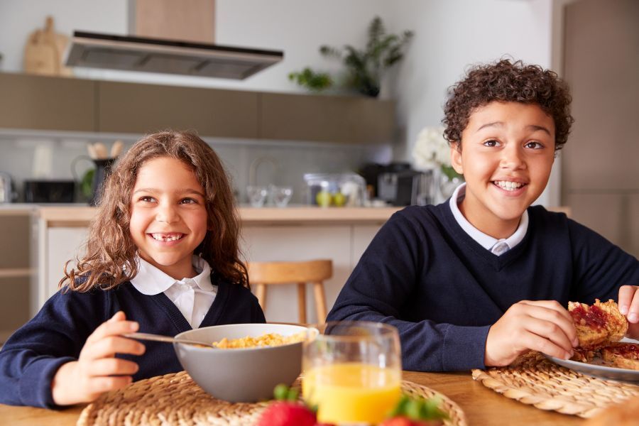 Children smiling eating breakfast in their school uniform