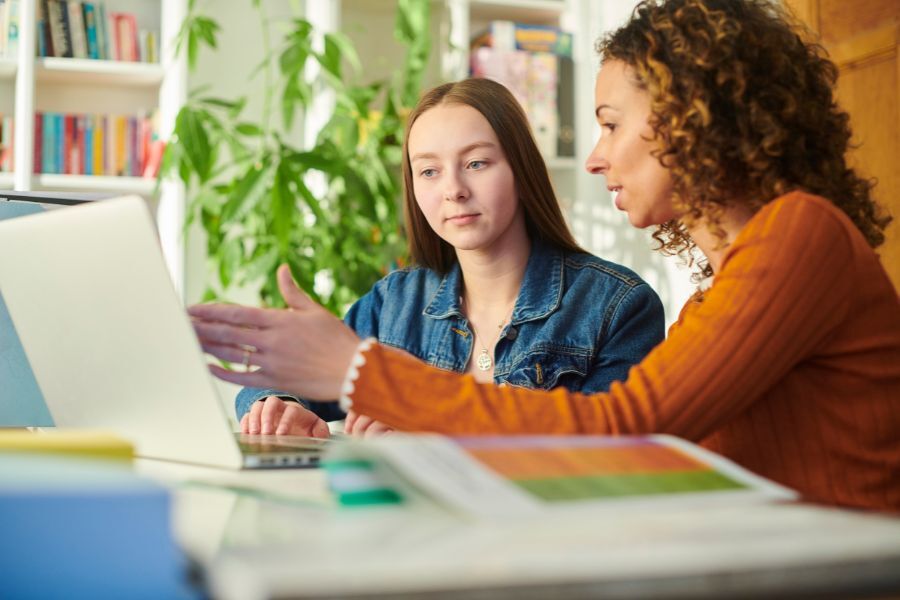 teenager talking to adult looking at laptop