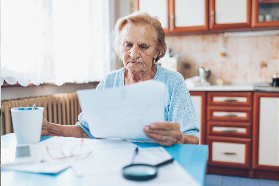 An elderly lady sat at a table looking at a bill or statement