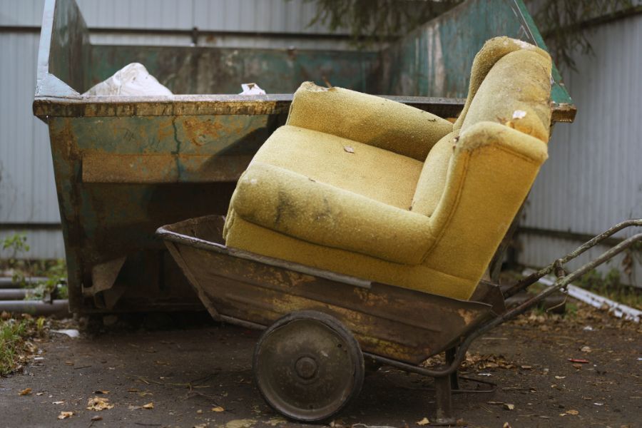 Sofa in a wheelbarrow near a skip