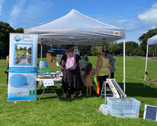 group of people stood under a gazebo in a park containing craft and games tables