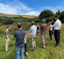 group of people stood in a field having a discussion, surrounded by vegetation and blue skies