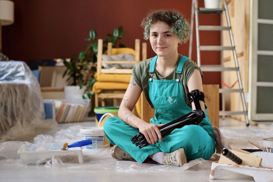 Young woman sitting on the floor surrounded by paints and DIY equipment holding a bionic arm