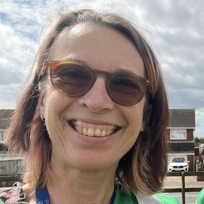 Women in sunglasses smiling with brown hair and a green hi-vis jacket and Exmouth Lanyard.