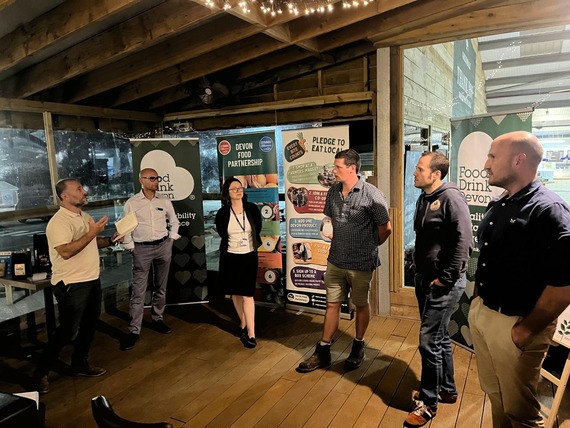 five white men and one white woman standing in a semi circle in front of banners, one of the men is speaking