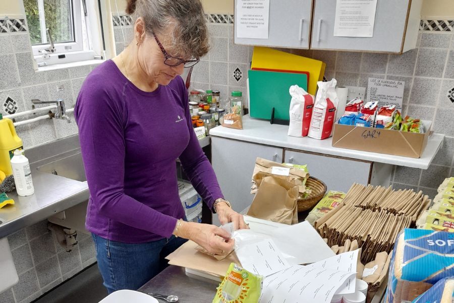 A volunteer, in a kitchen, putting labels on envelopes in a food packing programme