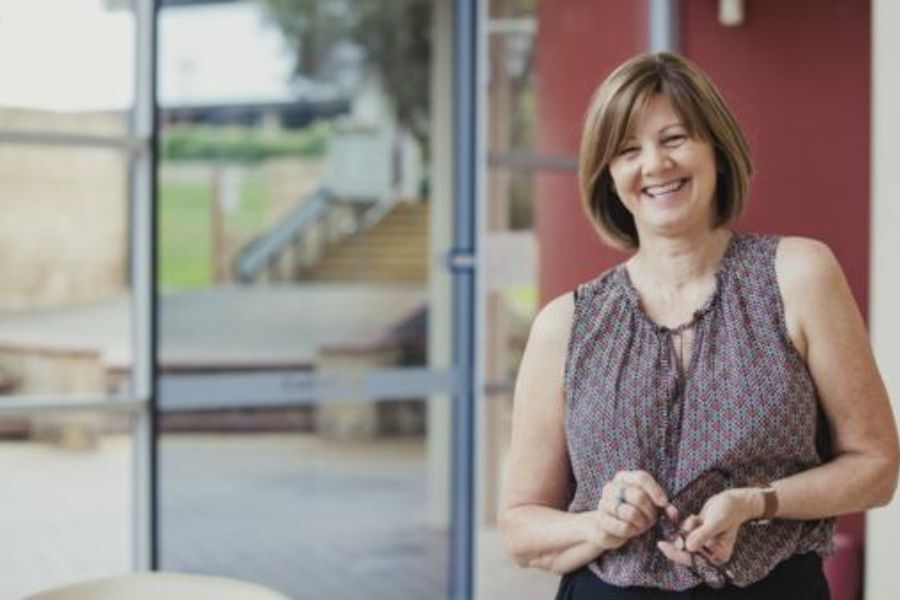 A lady smiling, stood in an open plan space with large glass windows behind her