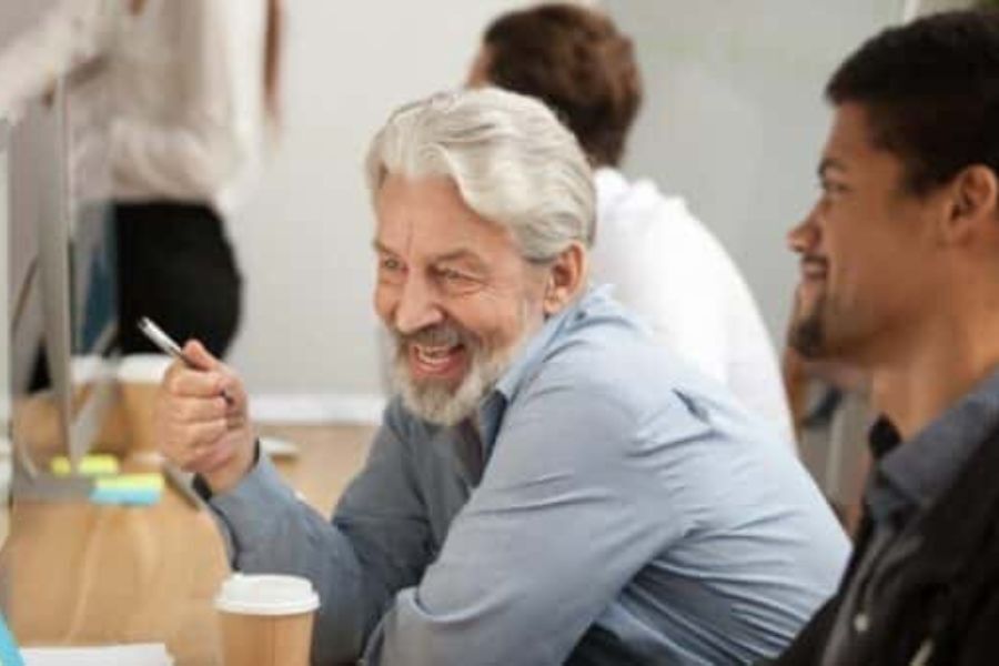 Two people sat working together at a laptop and screen, smiling and chatting