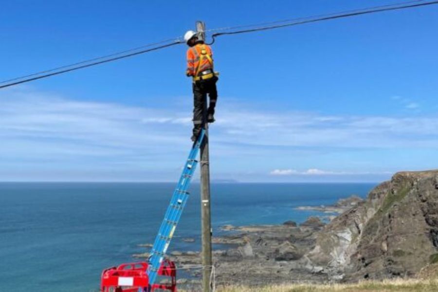 A man up a telegraph pole, working against a very blue clear sky