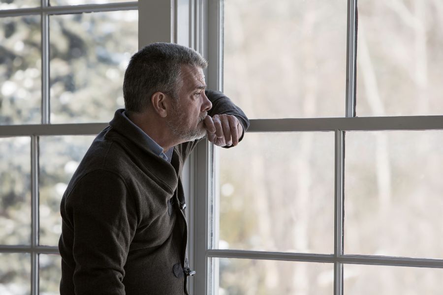 man looking out of window looking sad