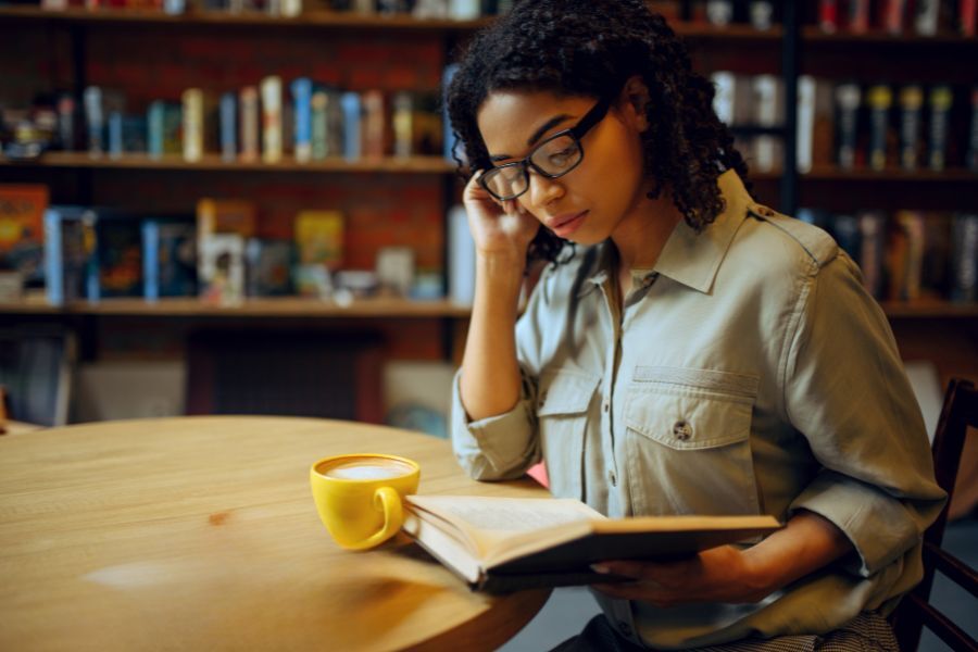 Woman sat with coffee reading book in library