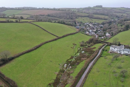 drone image of a field containing a stream above a village