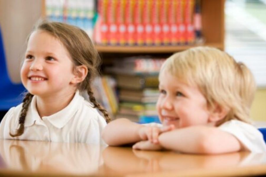 Two young children in Reception year at primary school, sat at a table smiling