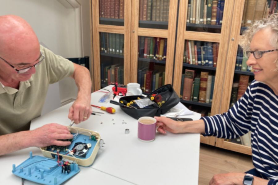 Two people sat at a desk fixing a piece of equipment