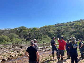 Group of people having a discussion in a field containing woody debris and standing water
