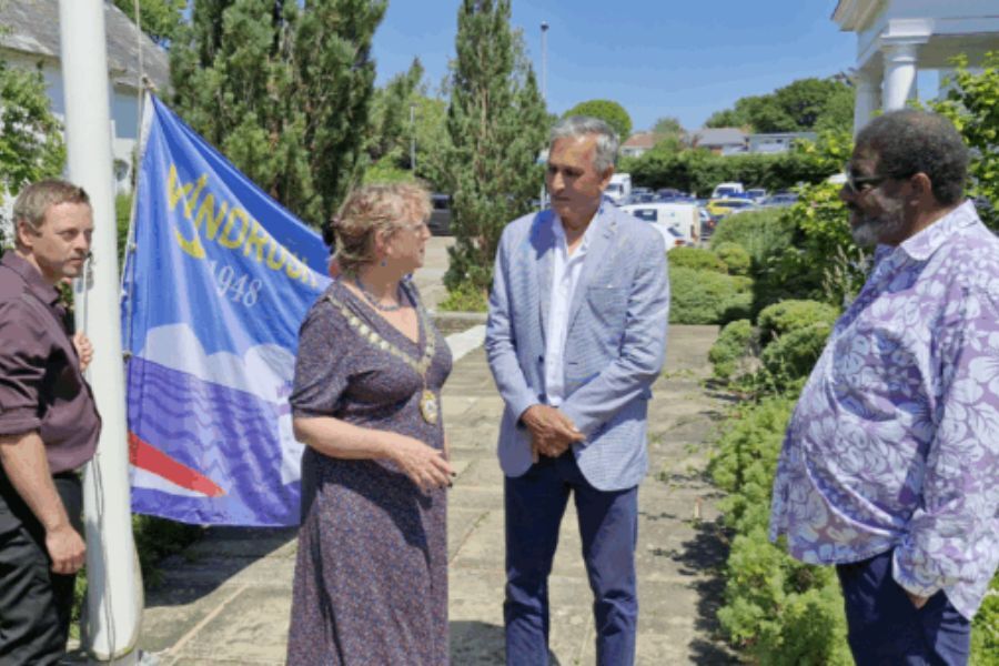 Devon County Council's Chair, Caroline Leaver, talking to Des Kumar and Dave Samuels in front of the Devon Windrush Flag at County Hall, Exeter