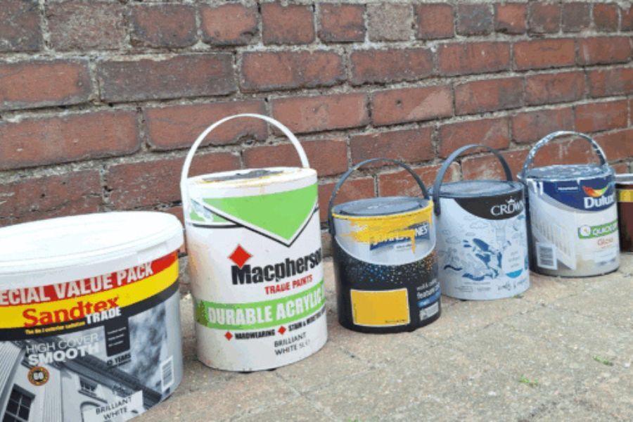 A line of paint pots on the pavement along a brick wall