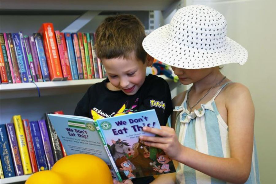 Two young children enjoying a book in front of book shelves in a library