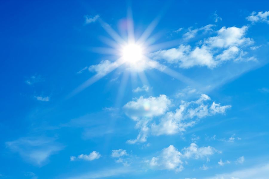 Bright sun in a blue sky with a few light clouds