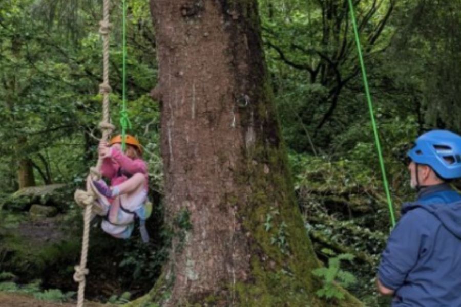A young girl swinging on a rope, supported by a member staff holding the rope