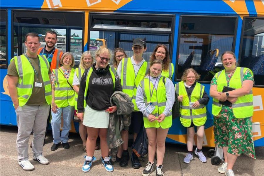 A group of people, adults and younger people, stood wearing high-visability jackets, in front of a parked bus