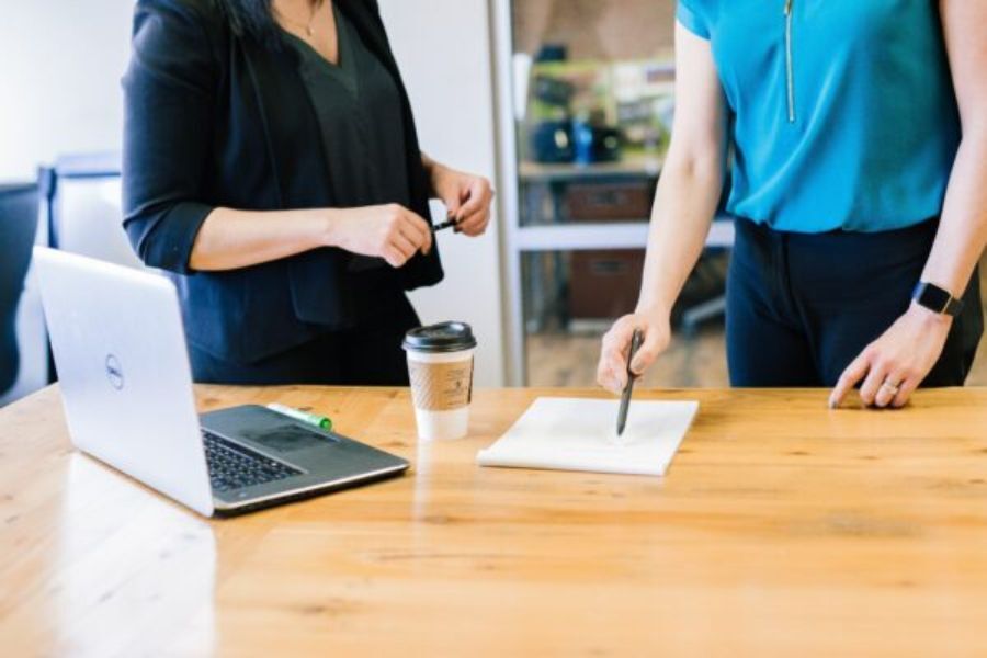 two people stood by a desk with a laptop on the desk. In view are the two people from desk-height to shoulders, but can't see their heads and faces