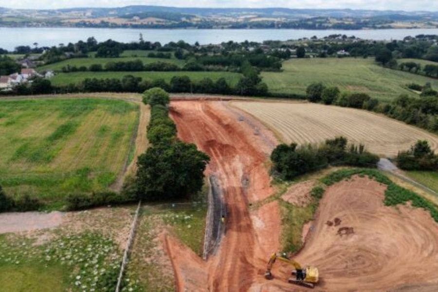 An aerial photograph above the work at Dinan Way. It shows a digger working on the ground with fields either side and the Exe Estuary in the distance
