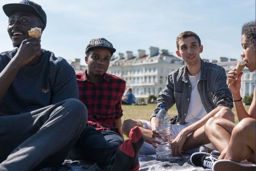 Young people sat having a picnic in a park, smiling