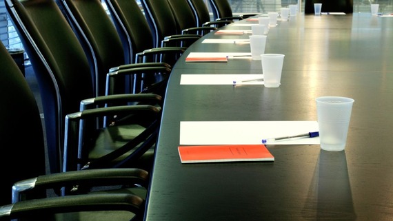Board table, with meeting papers in piles in each place. Seats are unoccupied