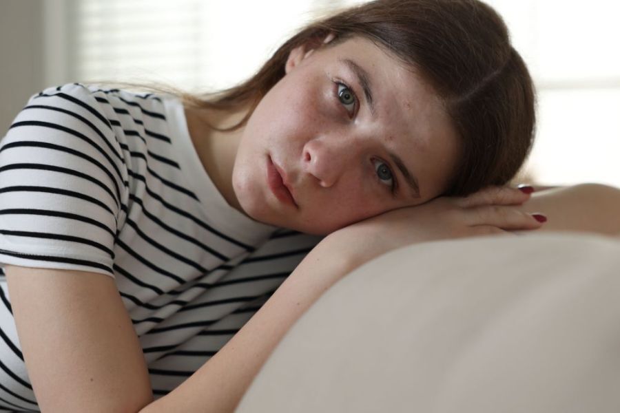 a teenage girl sat on her sofa at home with her head resting on the back of her hand. She is looking anxious