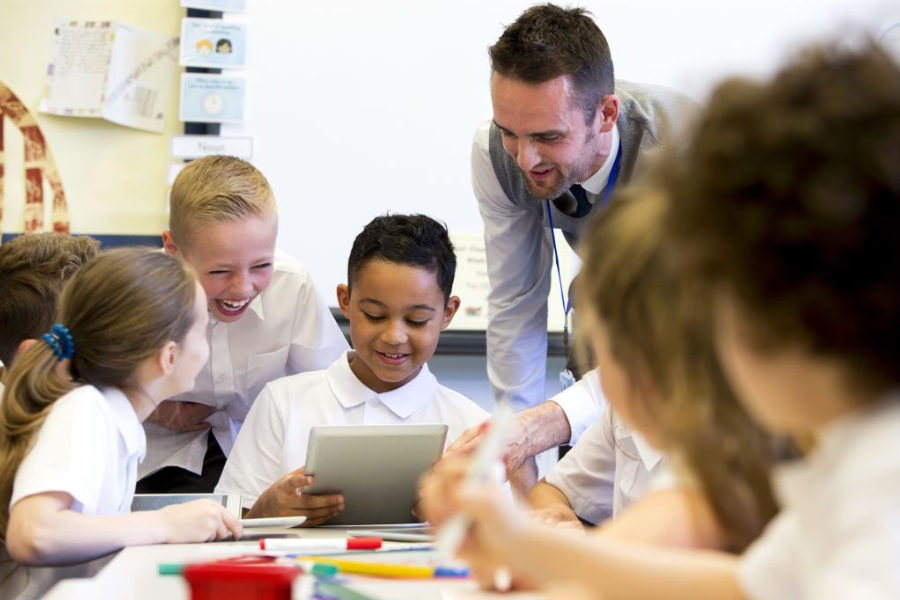 Students and an educator gathered around a table in a classroom, working together with a tablet and colourful stationary