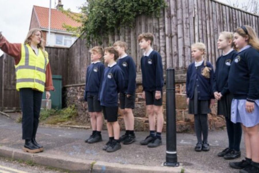 Primary school pupils taking part in the pedestrian safety training, walking along a pavement led by an adult in a high-vis jacket