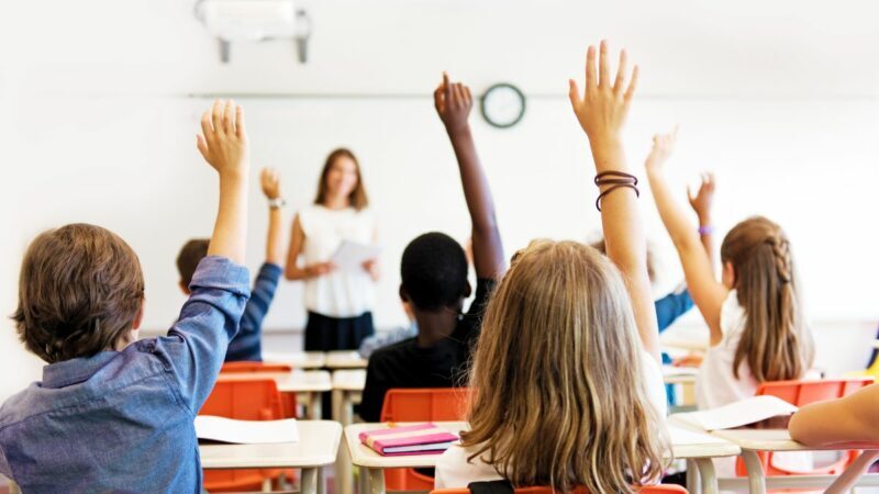 Classroom showing young people with raised hands and a teacher
