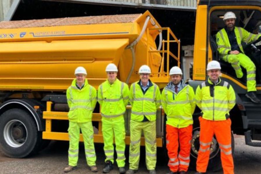 A crew of workers in high visibility clothing standing in front of a large gritting vehicle